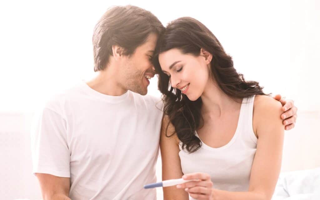 Una pareja sonríe mientras ella sostiene una prueba de embarazo